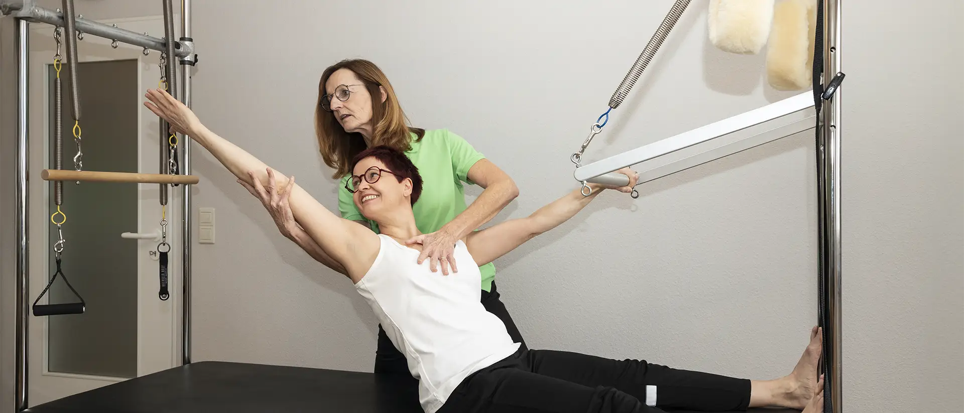 Patientin führt Pilates-Übung am Trainingsgerät unter Anleitung durch Patientin führt Pilates-Übung am Trainingsgerät unter Anleitung durch